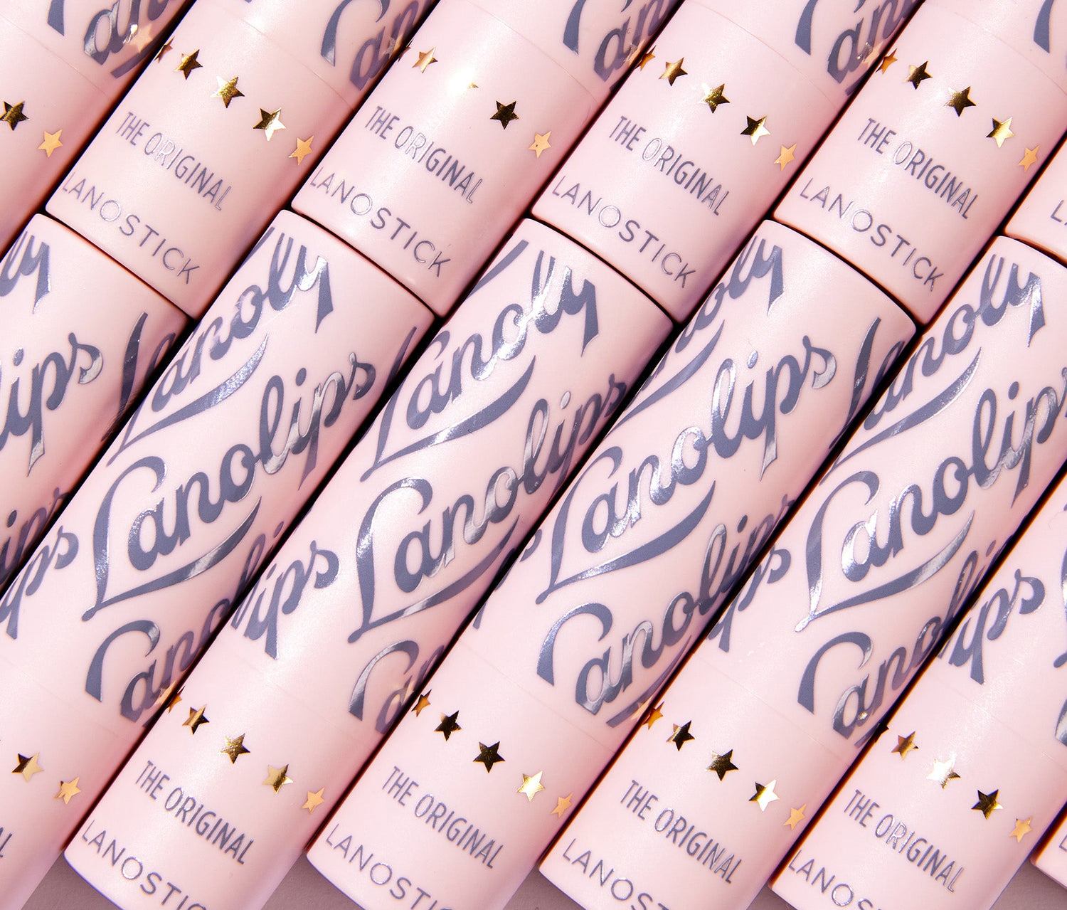 A close up of multiple Lanolips Lanostick tubes arranged in a diagonal pattern. This 90s-inspired wind-up lip balm is perfect for on-the-go hydration, fitting easily into pockets and bags. From the makers of the 'World’s Best Lip Balm,' Lanostick glides on smoothly, delivering a rich layer of moisture that deeply conditions lips. Formulated with lanolin, natural waxes, butters, and vitamin E, it nourishes and locks in hydration for hours. The ultimate day-balm for soft, healthy lips.