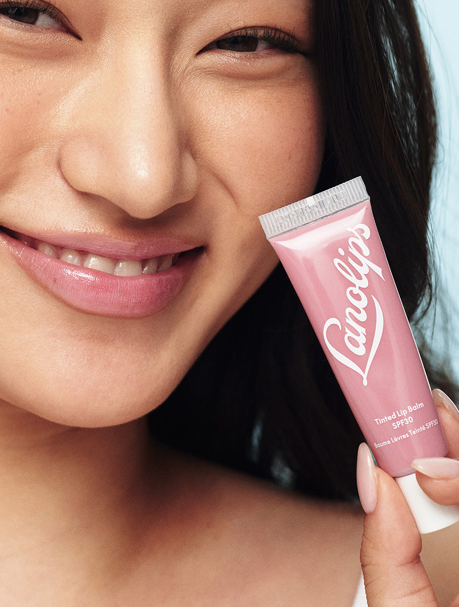 Model holding tube of Lanolips Tinted Lip Balm SPF30 in Rhubarb