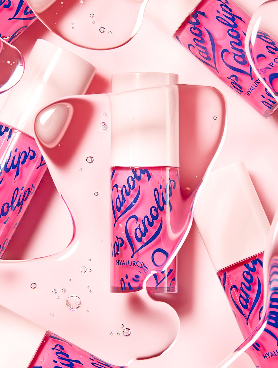 Lifestyle image of Lanolips Hyaluronic Lip Oils in Raspberry shade, arranged on a pink background with oil droplets and flowing lip oil for a dynamic, glossy effect