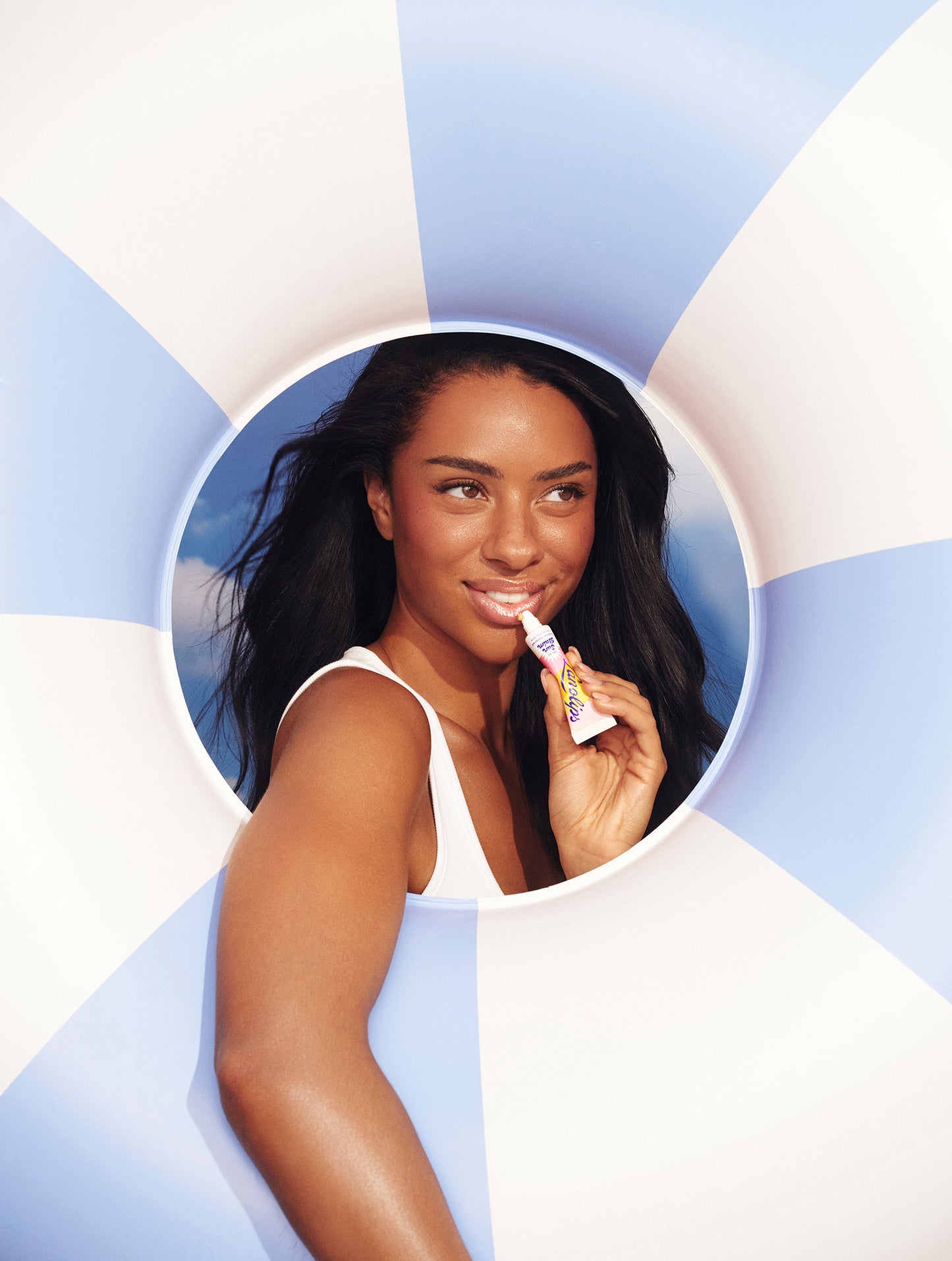 Model framed by a pool float applies Lanolips Sun Balm SPF 30 Tropical lip balm - hydrating, glossy, sun-safe lips with a tropical vibe.