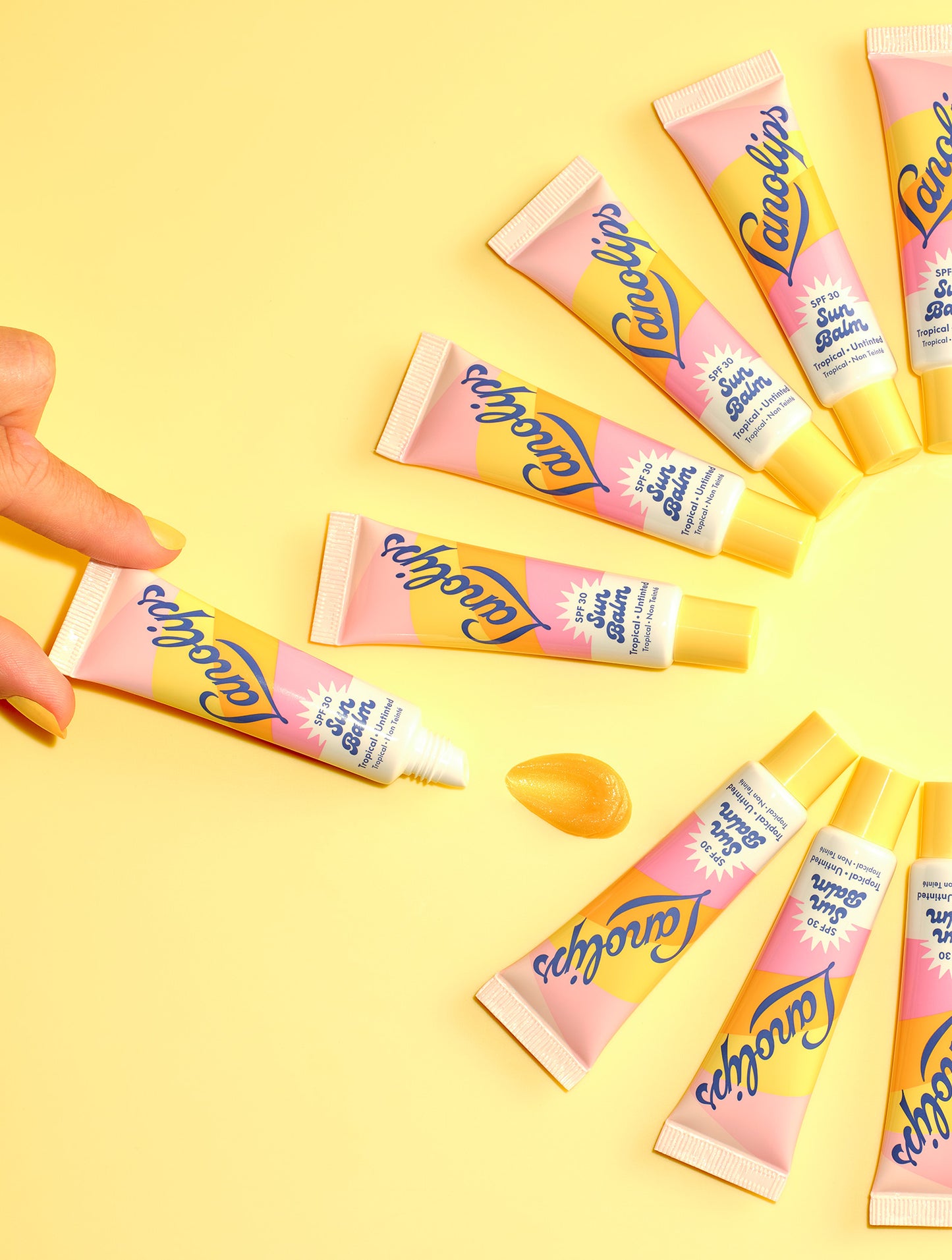 Tubes of Lanolips Sun Balm SPF 30 Tropical arranged in a sun shape on yellow. Hydrating, glossy, untinted SPF balm - your lips’ daily sun visor.