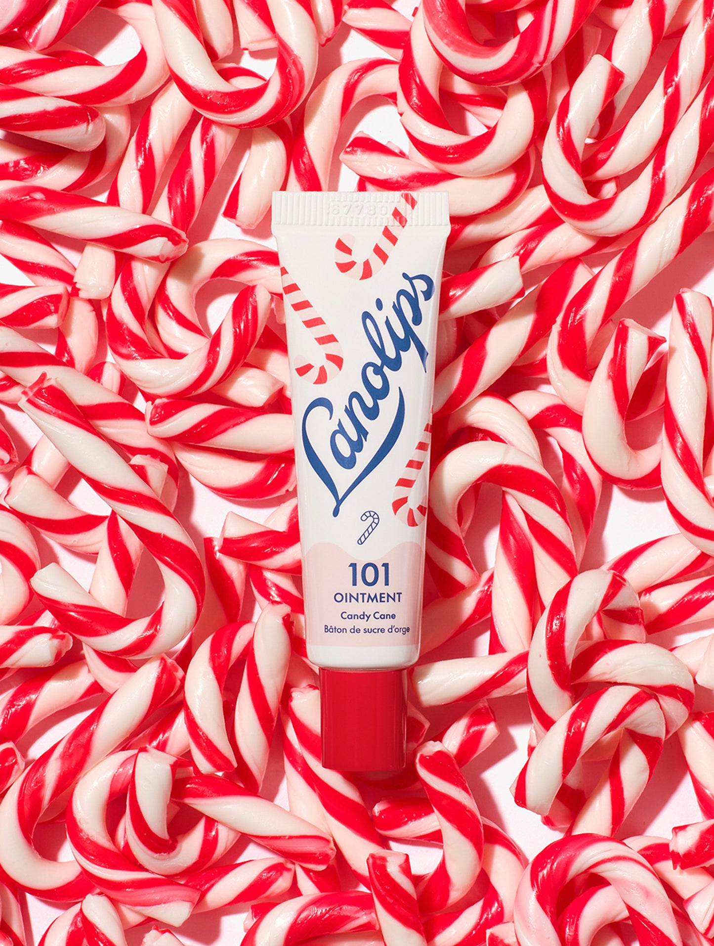Lanolips 101 Ointment Multi-Balm Candy Cane tube on a background of red and white candy canes. Made with all-natural lanolin, vitamin-e and sweeten peppermint flavour.