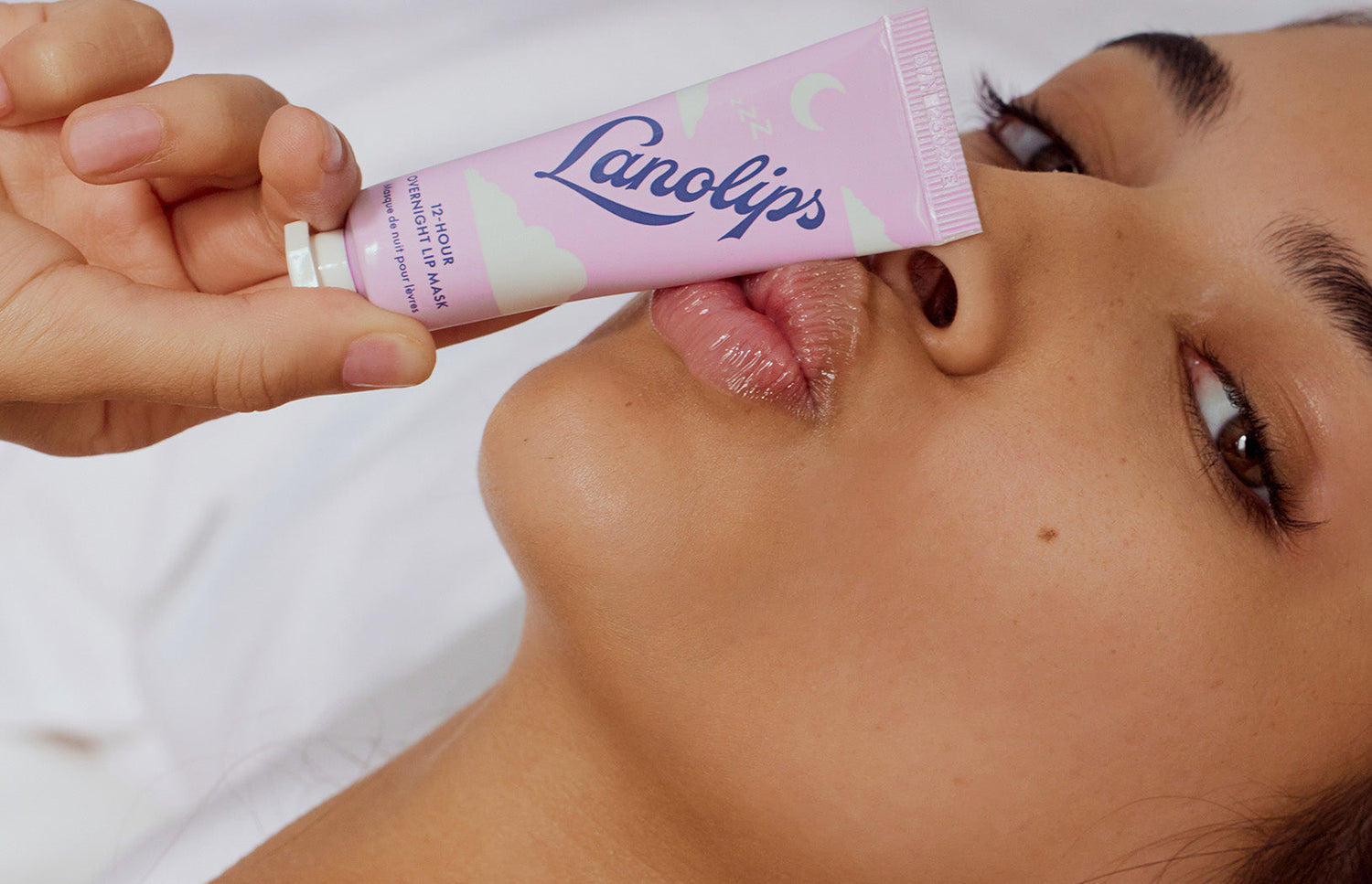 Close up of a model lying down, holding Lanolips 12-Hour Overnight Lip Mask to her lips. This content banner showcases Lanolips' ultra-hydrating, lanolin-powered lip mask designed for intense overnight repair. Enriched with natural ingredients, this cult-favourite product delivers soft, supple lips while you sleep. Perfect for dry, chapped lips in need of deep moisture and glow.