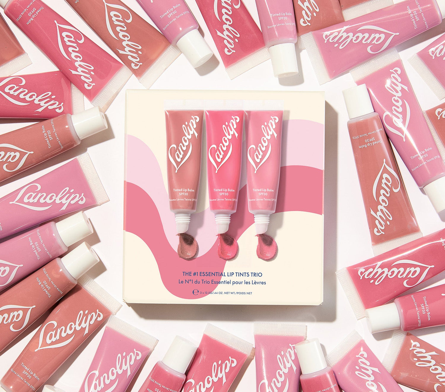 Lanolips The #1 Essential Lip Tints Trio displayed with pink tubes and swatches. This lanolin-rich set includes three bestselling tinted balms - Perfect Nude, Rhubarb, and Rose. Each balm delivers sheer colour, SPF30 protection, and intense hydration with over 70% lanolin. A cult all-in-one lip conditioner with beauty and brains.