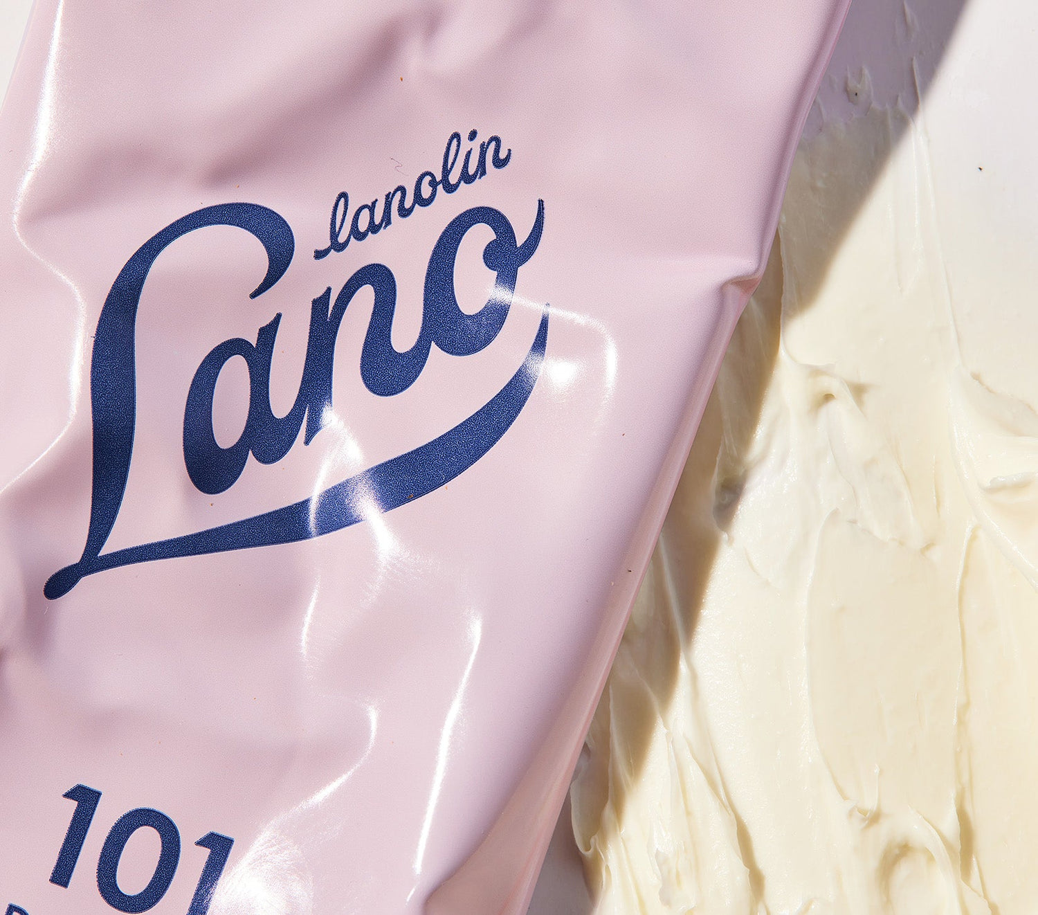 Close up of a pink tube of Lano 101 Dry Skin Super Cream on a rich, whipped texture. This dermatologically tested cream, with triple lanolin, deeply hydrates and locks in moisture. Its unique formula grips the skin before absorbing, creating a protective barrier. Clinically proven to boost hydration by 98% after one use, it’s perfect for dry, sensitive skin on the face, hands, and body.