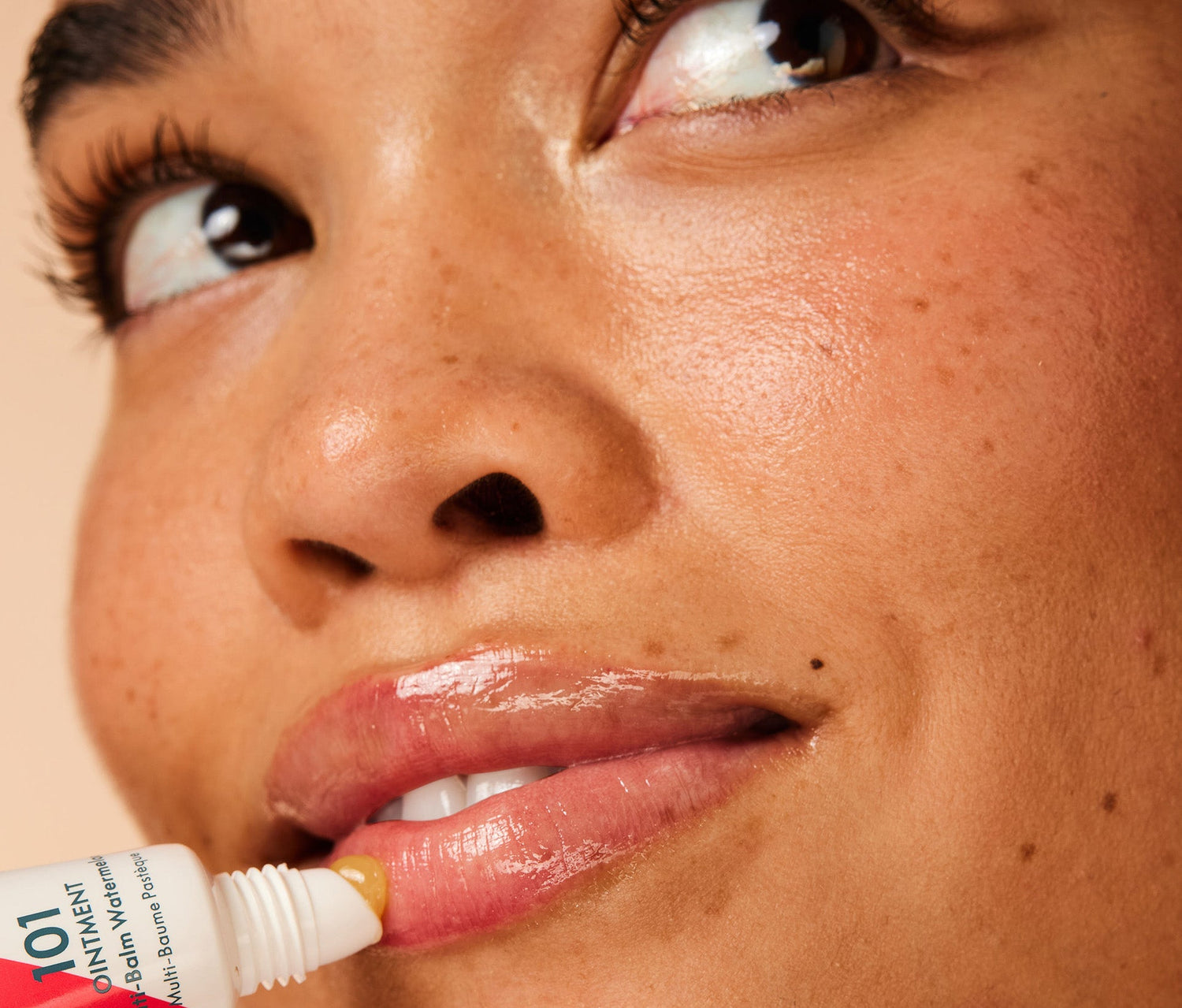 Close up shot of a model applying the Lanolips 101 Ointment Multi Balm in Watermelon to their lips. The super rich balm is made with lanolin, vitamin e and watermelon fruit extract to provide deep hydration to dry and chapped lips, elbows and cuticles.