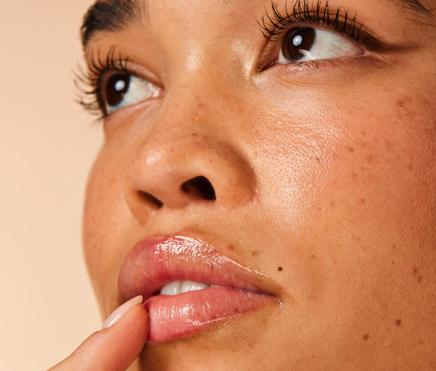 A close up shot of a model applying Lanolips 101 Ointment Multi Balm in Pear onto her lips, with a light peach background. Made with lanolin, vitamin e and pear seed oil to give long lasting hydration for dry and chapped lips.