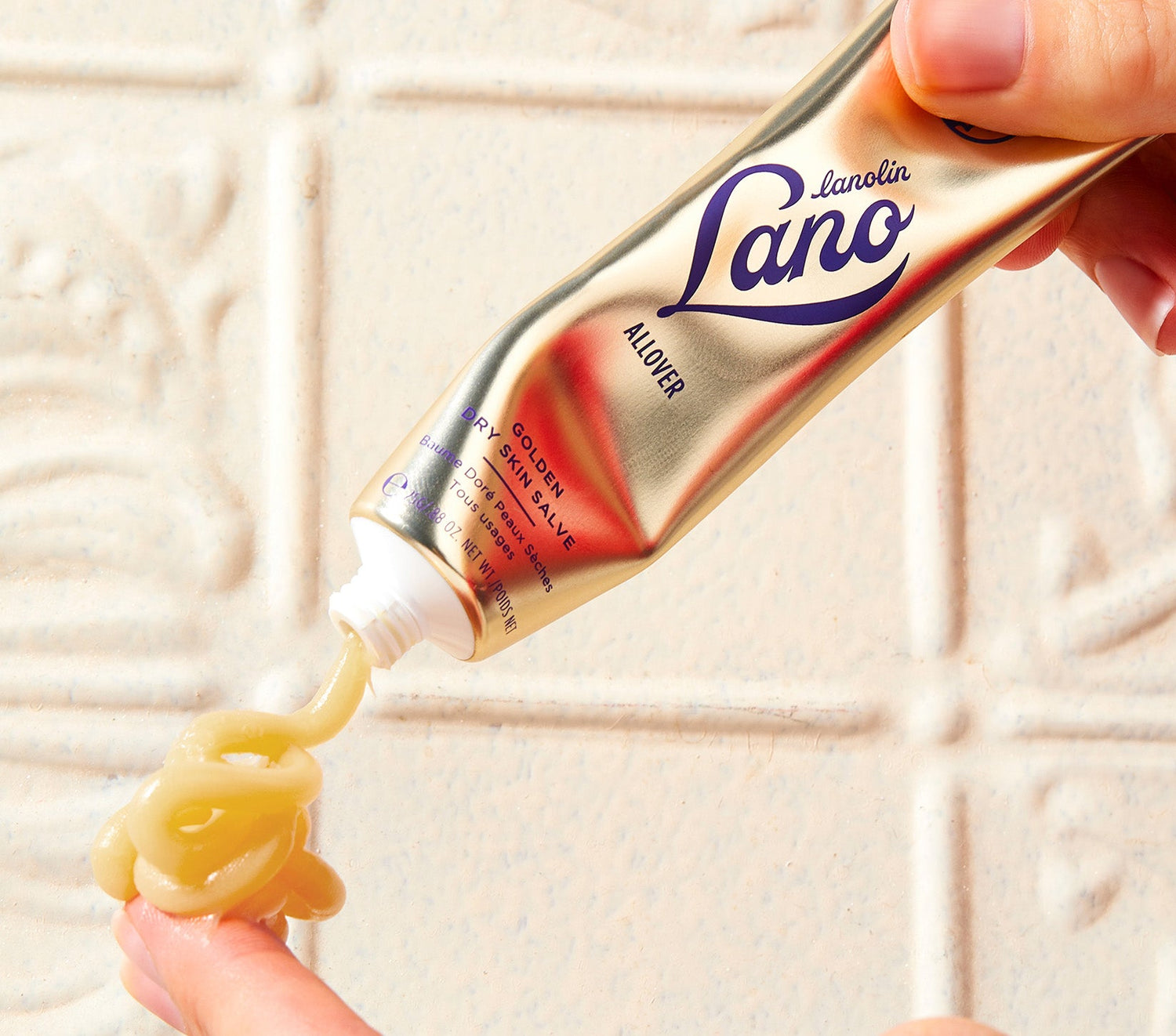 A tube of Lanolips Golden Dry Skin Salve is squeezed onto a fingertip, highlighting its rich, golden formula. Made with lanolin, Manuka honey, and vitamin E, this 100% natural balm intensely hydrates and protects dry skin for up to 48 hours. Perfect for rough hands, feet, legs, face, and lips- apply at night for soft, dewy skin by morning.