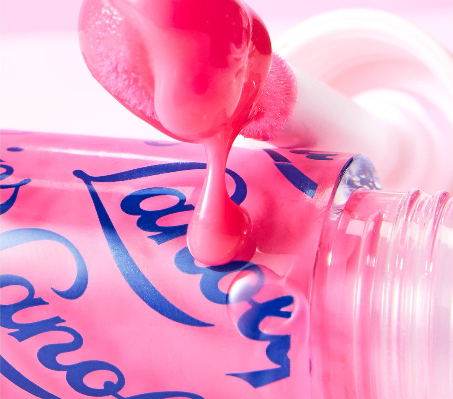 A close up shot of the Lanolips Hyaluronic Lip Oil Raspberry, with a fruity pink, glossy lip oil dripping from the plush jumbo applicator. The lip oil formula is infused with rich lanolin, hyaluronic acid and vitamin e provides long-lasting protection, making it a must-have for a low-maintenance, high-impact look.