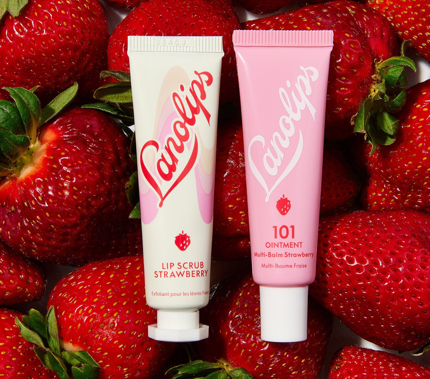 Lanolips Lip Rituals Scrub & Balm Strawberry Duo displayed on a bed of fresh strawberries. This lip care set includes the 100% natural Lip Scrub Strawberry, made with gentle sugar and real strawberry seeds to exfoliate dry lips, and the 101 Ointment Multi-Balm Strawberry, rich in lanolin for deep hydration. Step 1 in your lip routine, this duo smooths, softens, and reveals healthy, glowing lips. Housed in sustainable packaging with eco-conscious materials.
