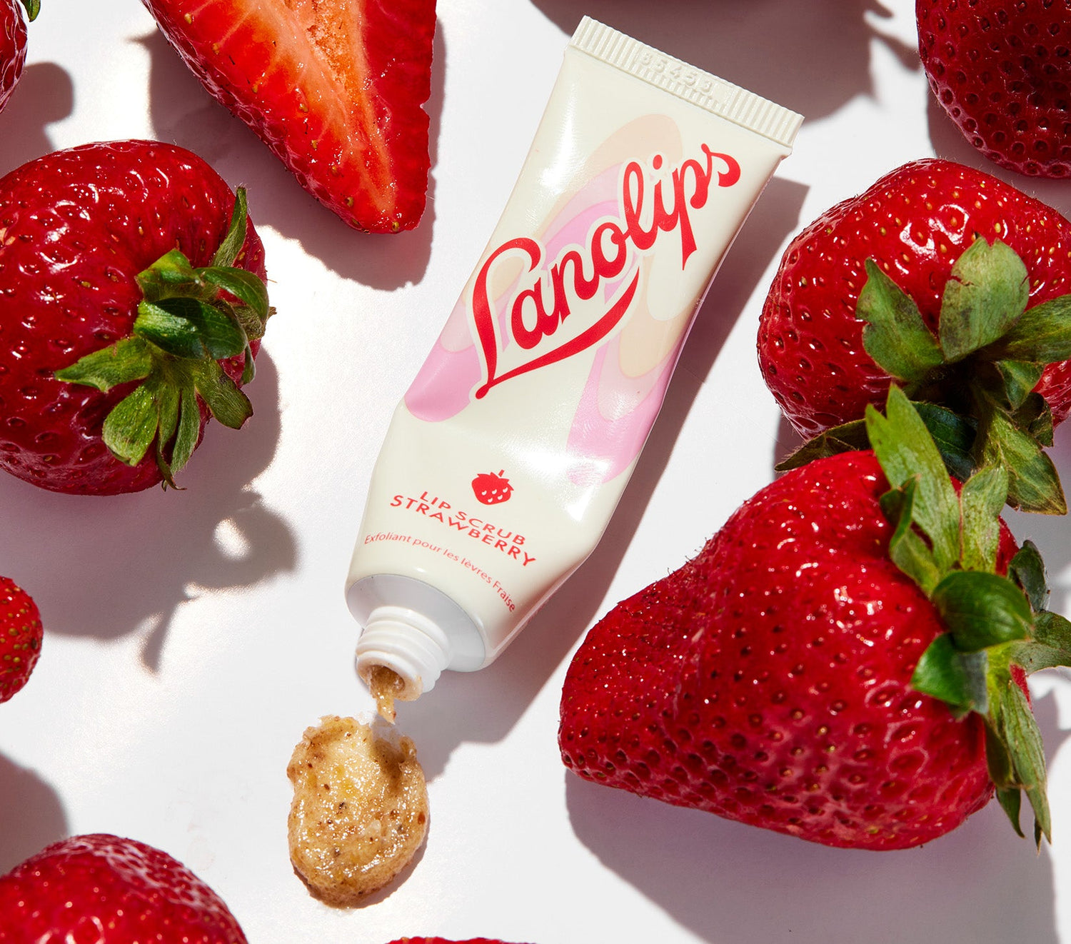 A tube of Lanolips Lip Scrub Strawberry rests among fresh, ripe strawberries, spilling onto a white surface. Lanolips’ Lip Scrub Strawberry is a 100% natural balm-based scrub made with gentle sugar and real, finely ground strawberry seeds to smooth away dry, flaky skin. The formula is enriched with 70% lanolin, instantly leaving lips soft and supple while revealing a healthy lip colour and natural glow.