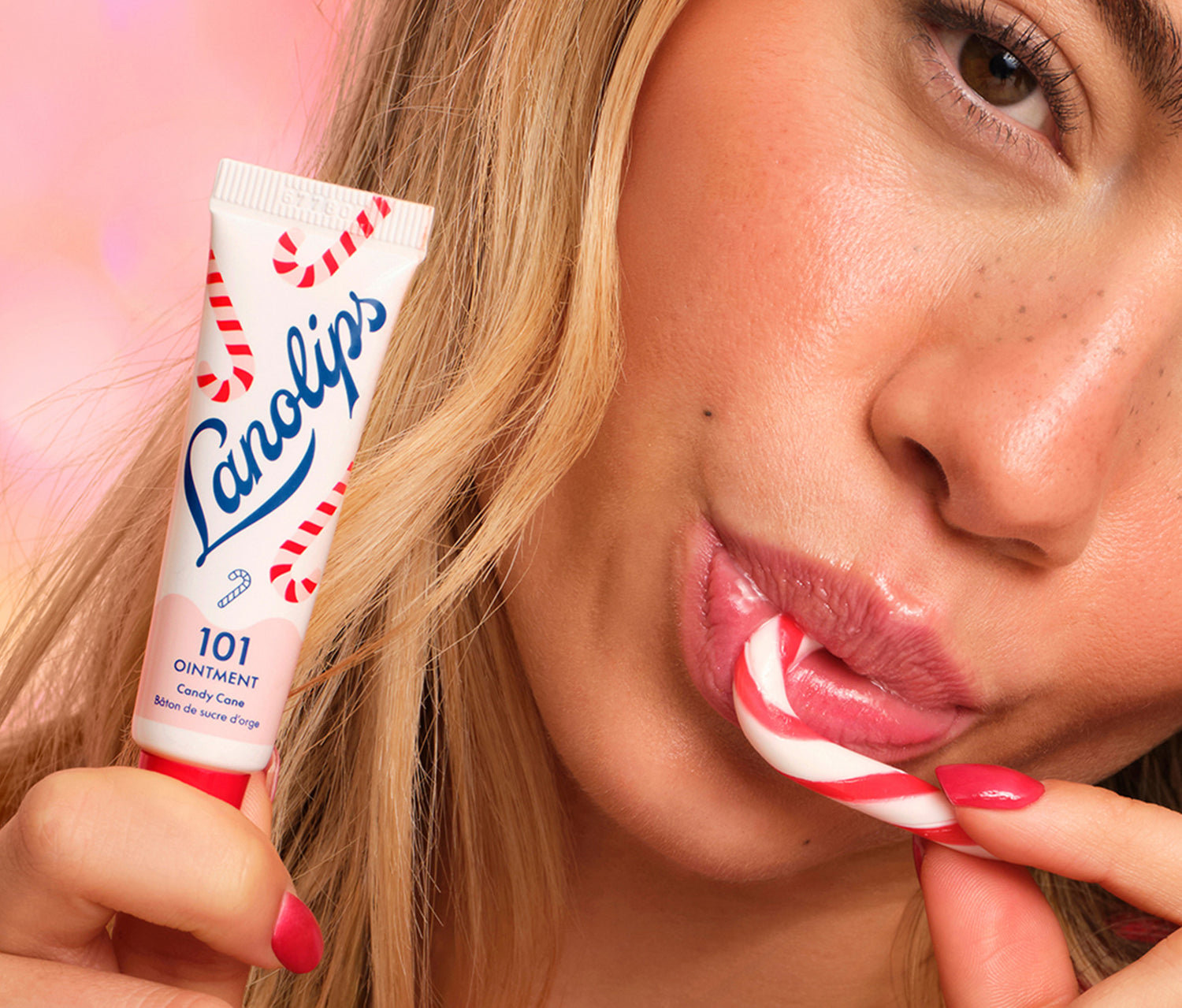 Model applying Lanolips 101 Ointment Multi-Balm Candy Cane lip balm to her lips with a pink background.