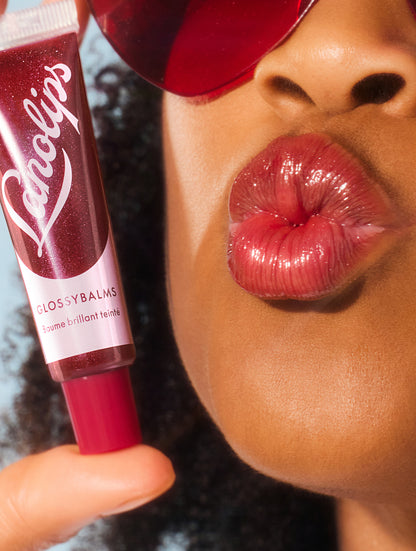 Close up image of a model holding a tube of lanolips glossy balms berry lip balm.