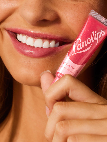 Close up image of a model holding a tube of lanolips glossy balms candy lip balm.