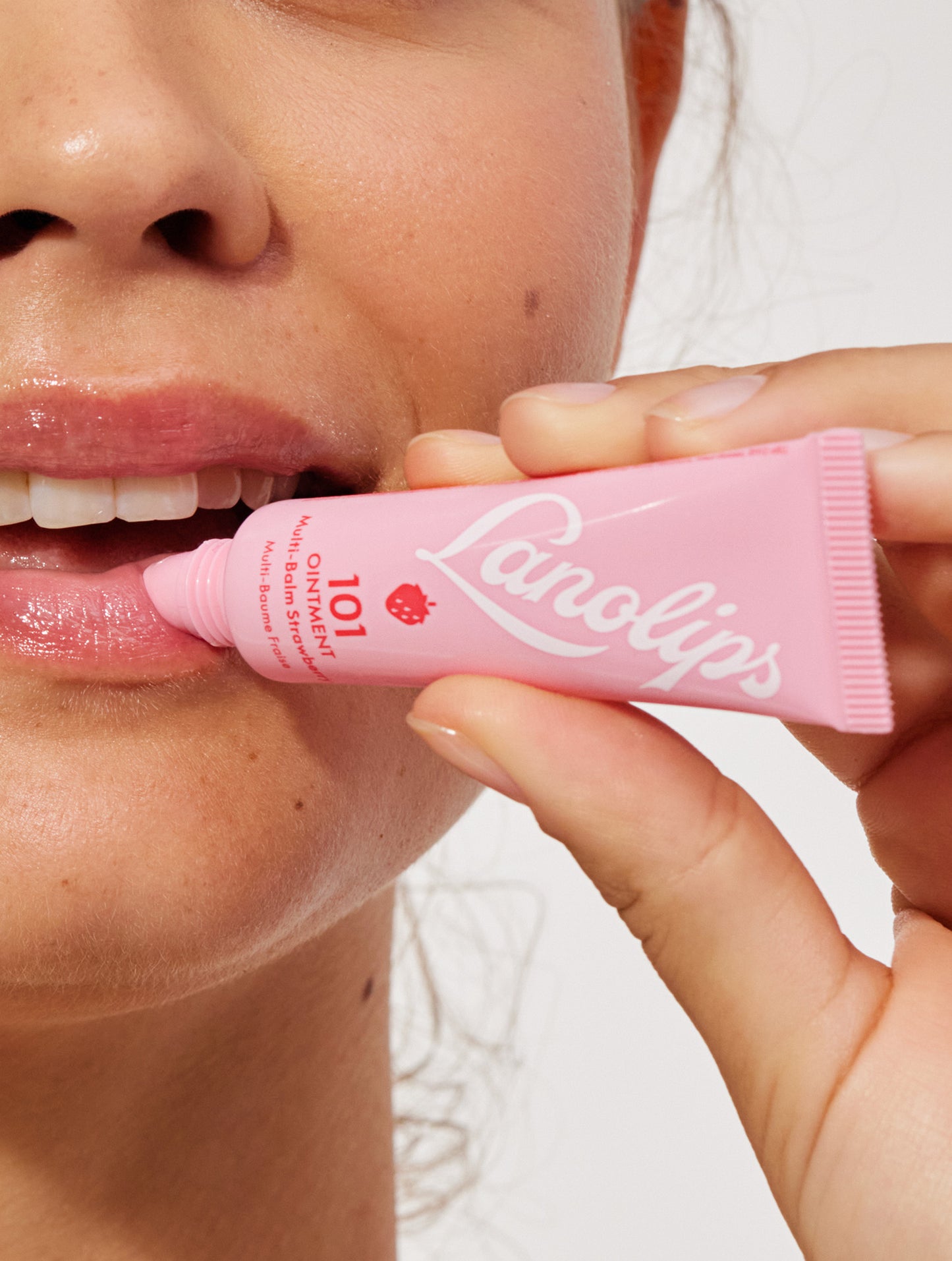 Model's hand holding a lanolips 101 ointment strawberry lip balm in her hand applying it to her lips.