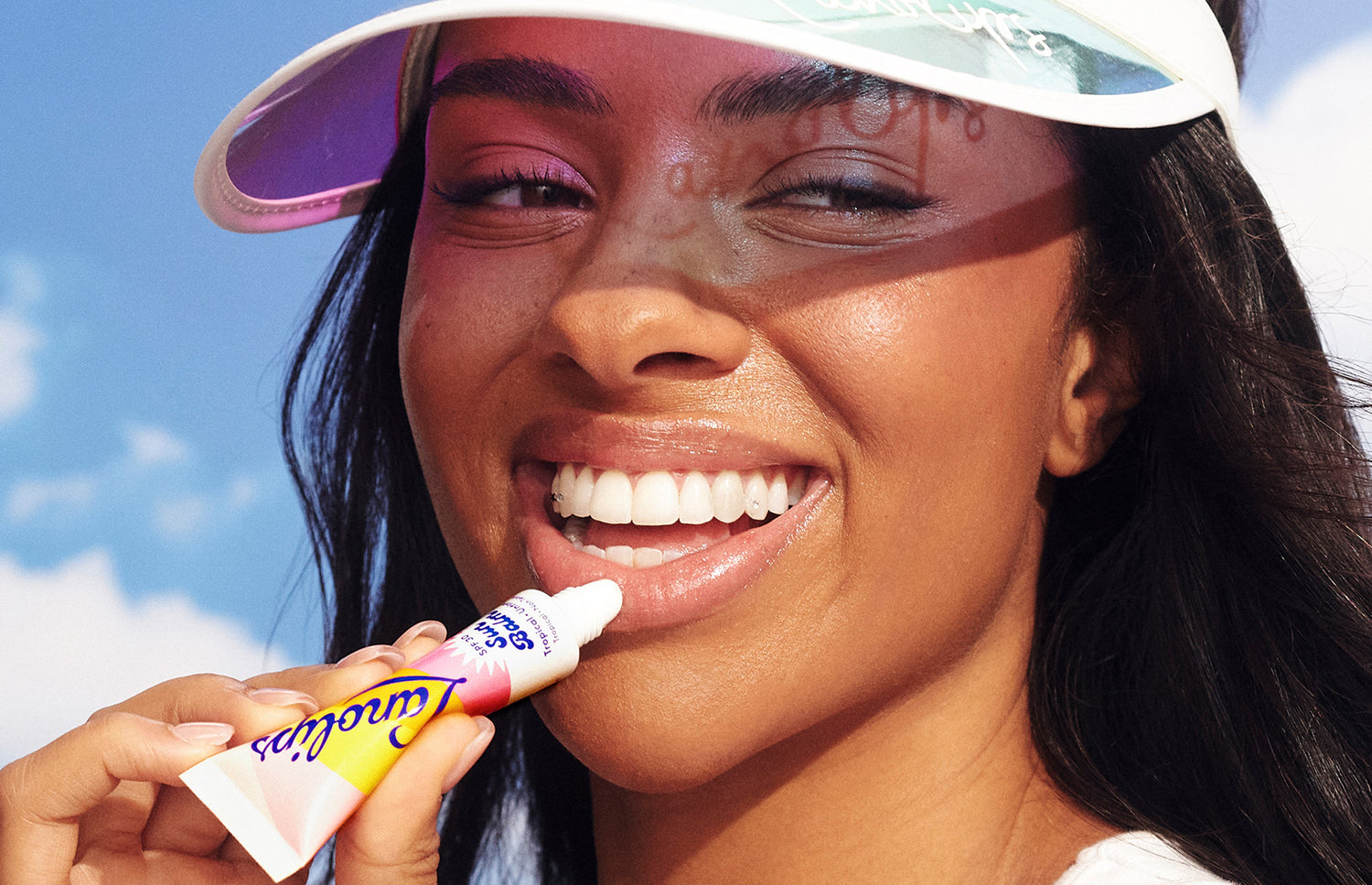 Model applying Lanolips Sun Balm SPF 30 Tropical untinted lip balm on her lips. Made with hydrating lanolin, vitamin e, shea butter and SPF, it's a sun in a tube.