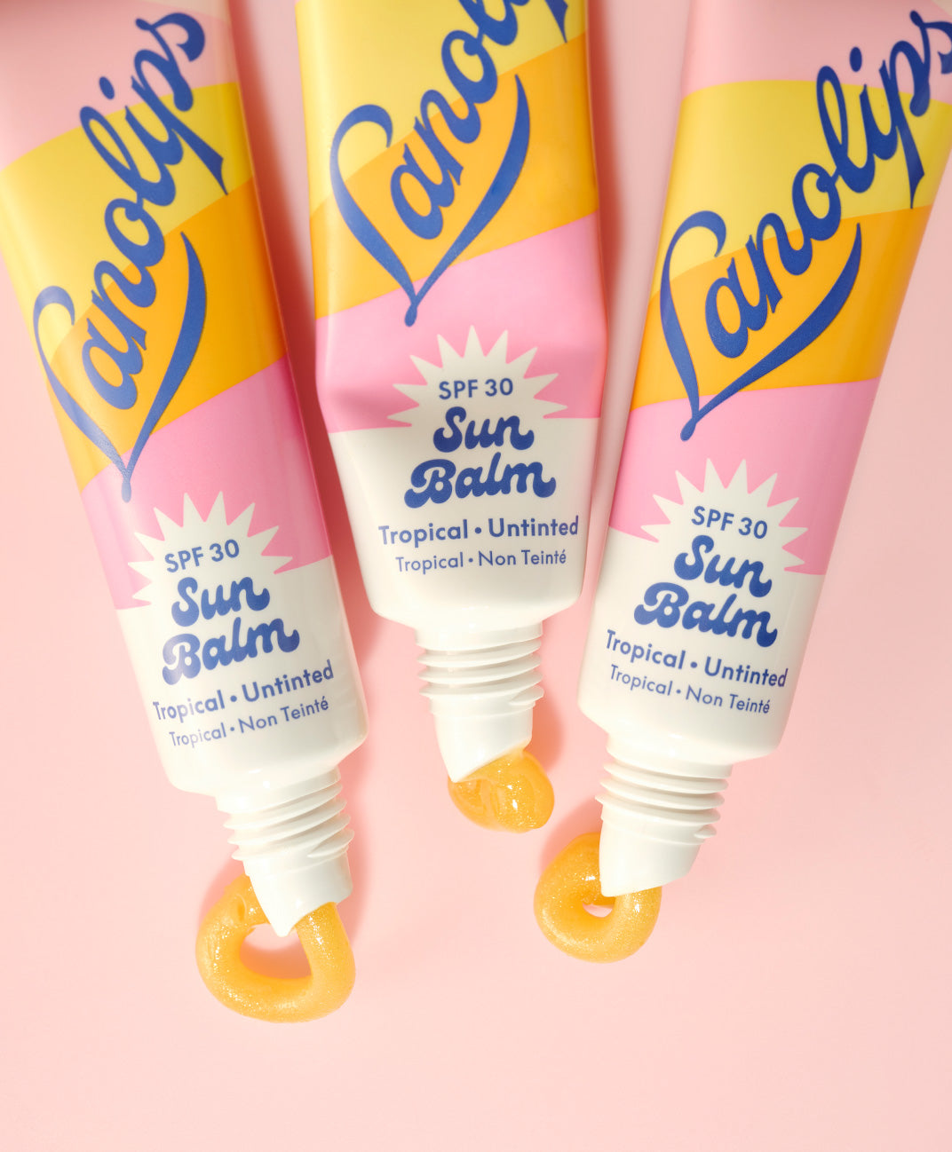 Close up shot of three squeezed tubes of the Lanolips Sun Balm SPF 30 Tropical lip balm against a pink background. The product shows a creamy, radiant formula is packed with hydrating lanolin, SPF protection, and a luminous sheen.