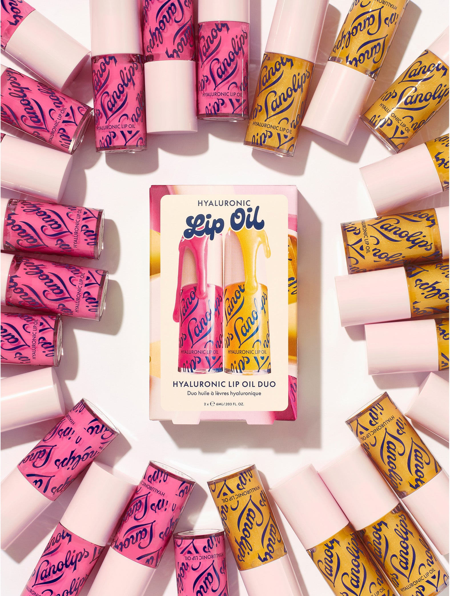 Lifestyle shot of the Lanolips Hyaluronic Lip Oil Duo in raspberry and honey, with product box surrounded by lip oil tubes.  