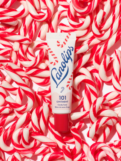 Lanolips 101 Ointment Multi-Balm Candy Cane tube on a background of red and white candy canes. Made with all-natural lanolin, vitamin-e and sweeten peppermint flavour. 