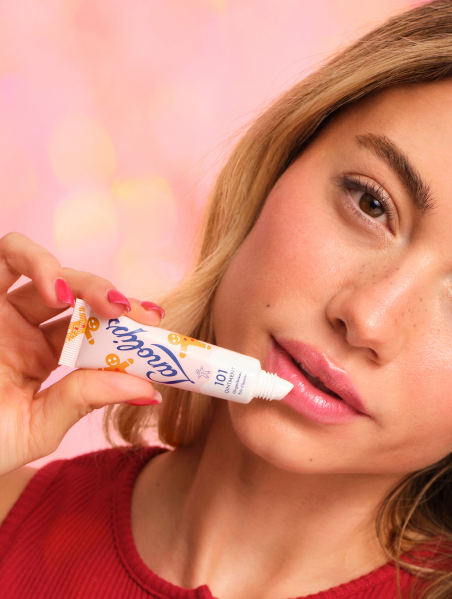 Model applying Lanolips 101 Ointment Multi-Balm Gingerbread lip balm to her lips with a pink background. Embrace warm spice and soft lips with this limited edition festive 101 Delicious Holiday gourmand flavour. 