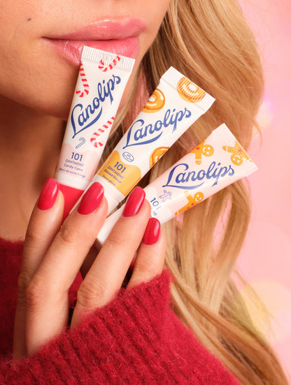 Close-up of model holding Lanolips Holiday Mini Bites lip balm trio in Candy Cane, Gingerbread and Glazed Donut flavours, with glossy lips and red nails.